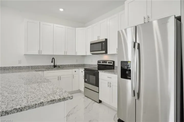 Kitchen with white cabinetry, appliances with stainless steel finishes, light stone counters, and sink