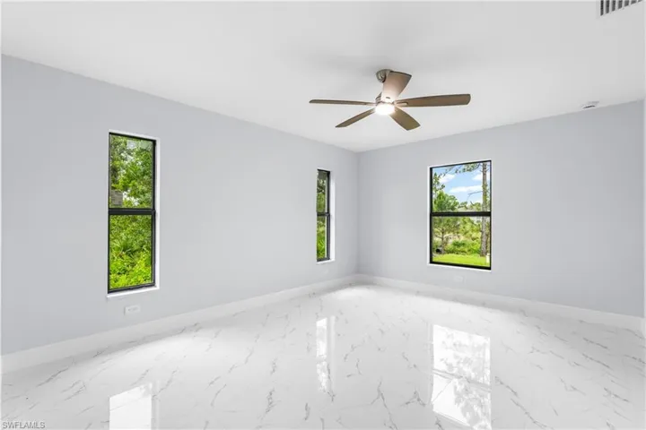 Spacious interior featuring reflective tile flooring, multiple windows providing abundant illumination, and a ceiling fan with integrated lighting