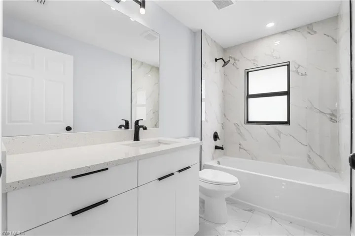 Modern bathroom featuring a white vanity with a light-toned countertop, a black single-handle faucet, and a large wall-mounted mirror