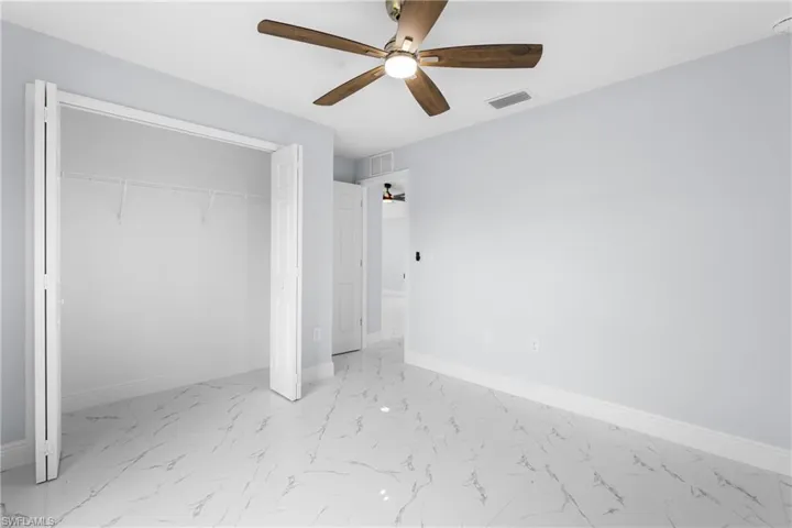 Spacious room featuring large format tile flooring, a ceiling fan with wood-finish blades, light-toned wall paint, and bi-fold closet doors with built-in shelving