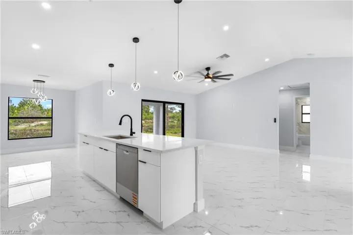 Open-concept interior featuring large format marble-look tile flooring, a central kitchen island with a built-in stainless steel dishwasher, modern pendant lighting, a black ceiling fan, and recessed lighting