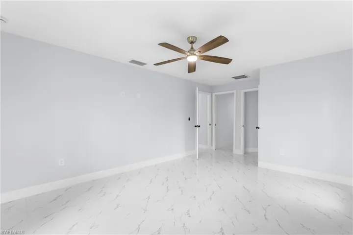 Spacious room featuring white large format tile flooring, light blue walls, and a wood-finish ceiling fan with integrated lighting