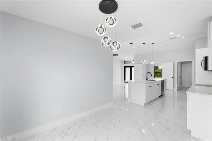 Open-concept kitchen and living area featuring a modern chandelier, white shaker cabinetry, an island with a black gooseneck faucet, stainless steel appliances, and large format white tile flooring