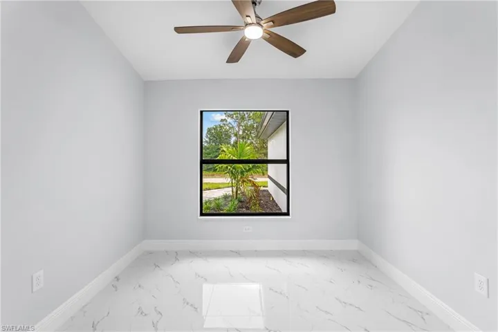 Bright interior space featuring a window with black trim, a ceiling fan with wood-finish blades, pristine white walls, and a white marble-look tile floor