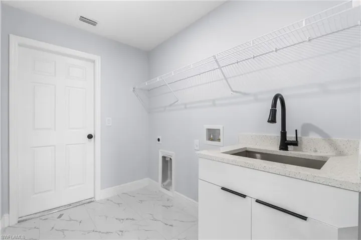 Utility room featuring white cabinetry, a light-toned countertop, an undermount sink with a black faucet, and white wire shelving