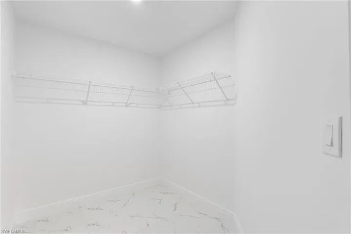 Corner closet space featuring wire shelving, white baseboards, and marble-look tile flooring