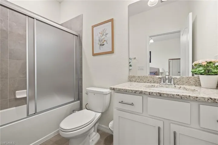 Full bath featuring vanity, toilet, enclosed tub / shower combo, and a textured wall