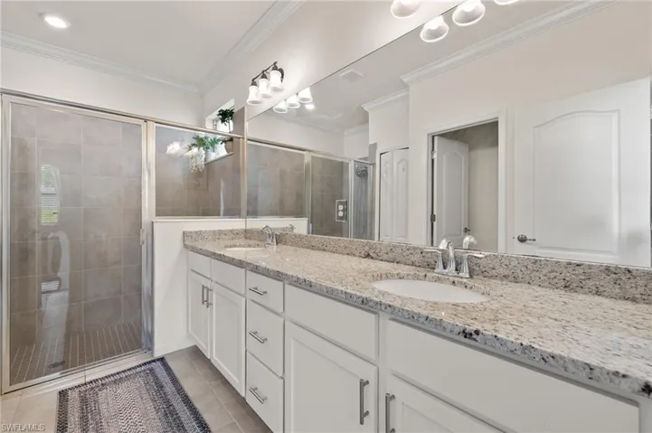 Bathroom featuring double vanity, a stall shower, ornamental molding, and tile patterned floors