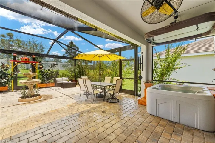 View of patio / terrace featuring a lanai, ceiling fan, a hot tub, and outdoor dining space