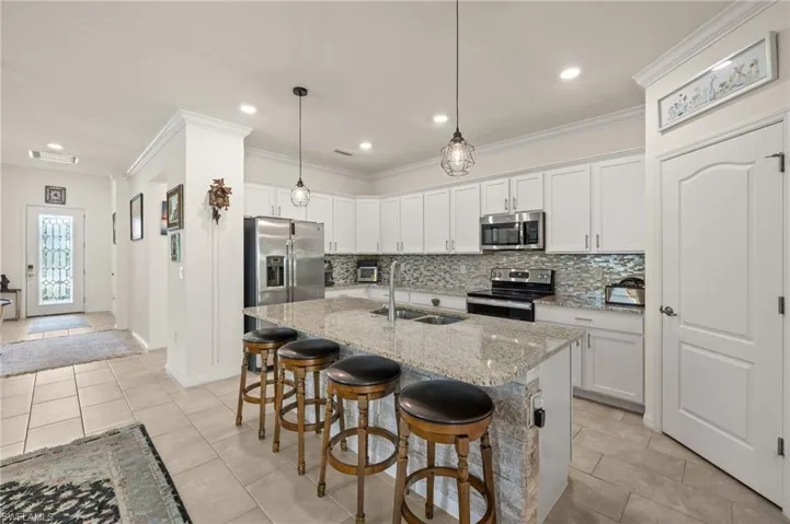 Kitchen with stainless steel appliances, a double sink, backsplash, crown molding, and a breakfast bar area.