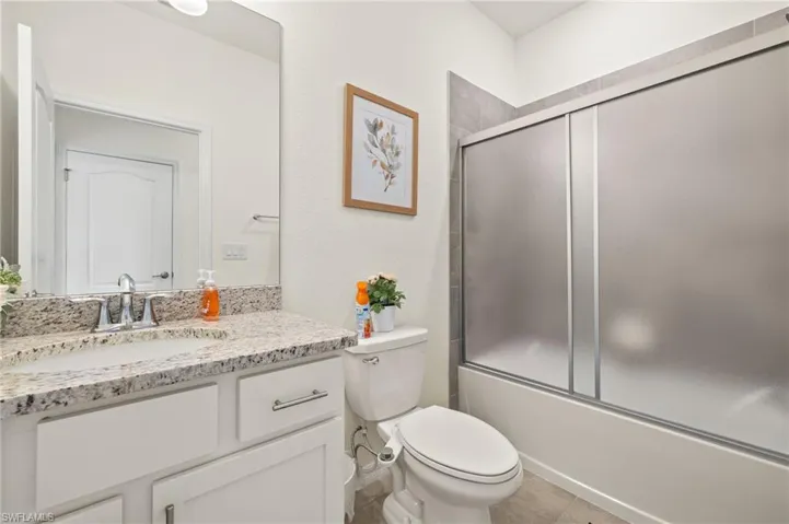 Bathroom featuring vanity, toilet, bath / shower combo with glass door, and tile patterned flooring