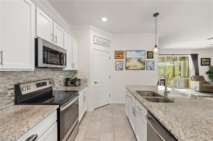 Kitchen with stainless steel appliances, a sink, natural stone backsplash & white cabinets.