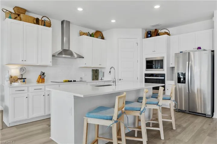 Kitchen featuring white cabinetry, center island with stone-surface countertop, stainless steel appliances, stainless steel range hood, and wood-finish flooring