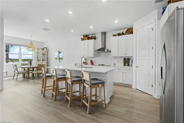 Kitchen featuring white shaker-style cabinetry, quartz countertops, a stainless steel range hood, recessed lighting, and wood-finish flooring