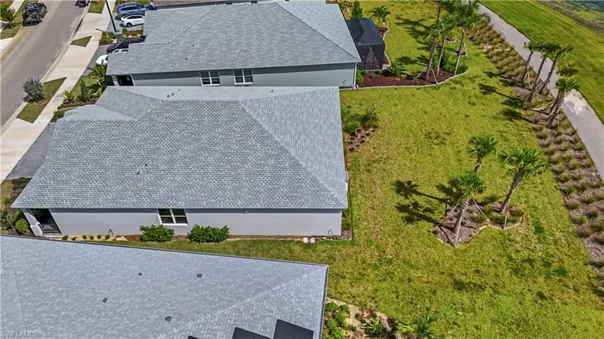 Aerial perspective of a property lot featuring an expansive lawn, established palm tree landscaping, and a paved walkway bordering the perimeter