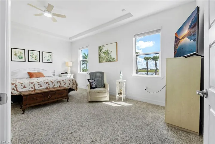 Room featuring a tray ceiling, neutral wall-to-wall carpeting, and a multi-blade ceiling fan with integrated lighting