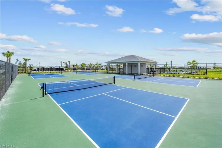 Multi-court pickleball facility with blue surfacing, perimeter chain-link fencing, and a covered pavilion structure