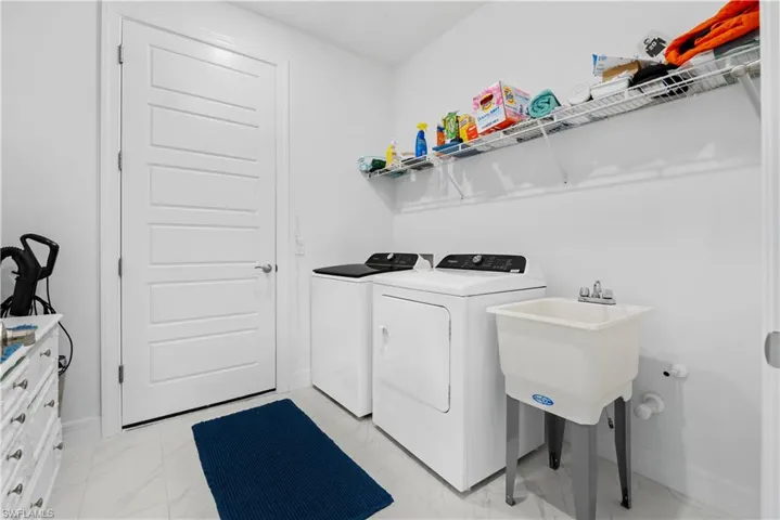 Utility room featuring white tile flooring, a wall-mounted wire storage shelf, and a freestanding utility sink