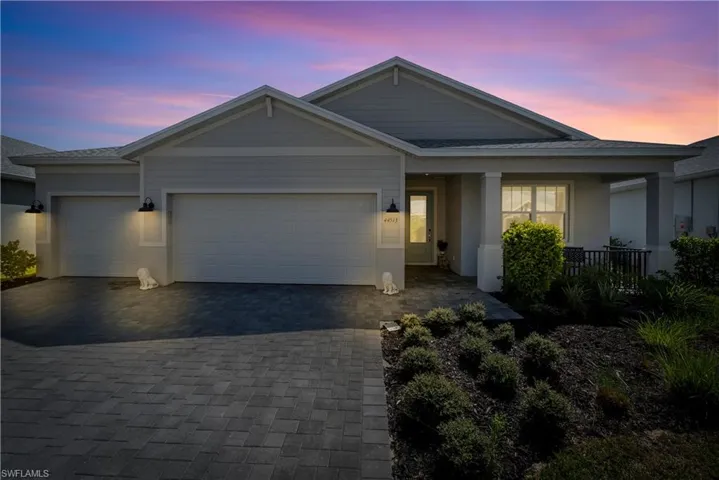Single-story residence featuring a multi-gable roofline, neutral siding, attached two-car garage, covered entryway, and paver driveway