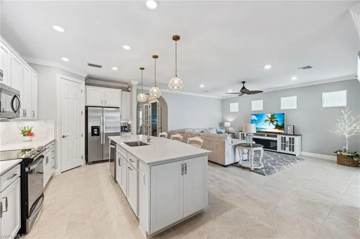 Kitchen with a kitchen island with sink, white cabinetry, stainless steel appliances, sink, and ceiling fan