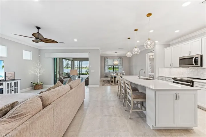 Kitchen featuring a center island with sink, pendant lighting, decorative backsplash, ceiling fan, and electric stove