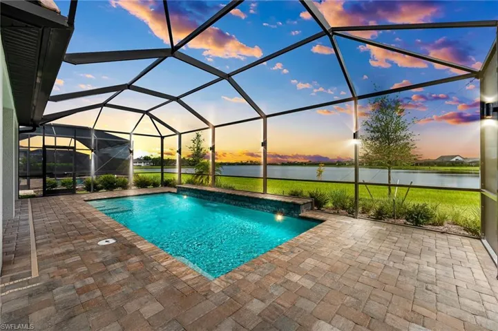 Pool at dusk featuring glass enclosure, a water view, a patio, and pool water feature