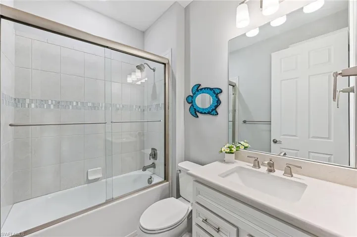 Full bathroom with enclosed tub / shower combo, toilet, and vanity
