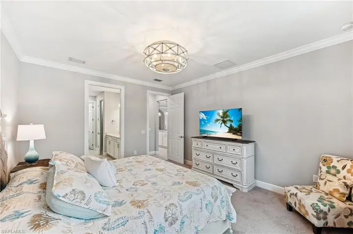 Carpeted bedroom with crown molding, ensuite bath, and a chandelier