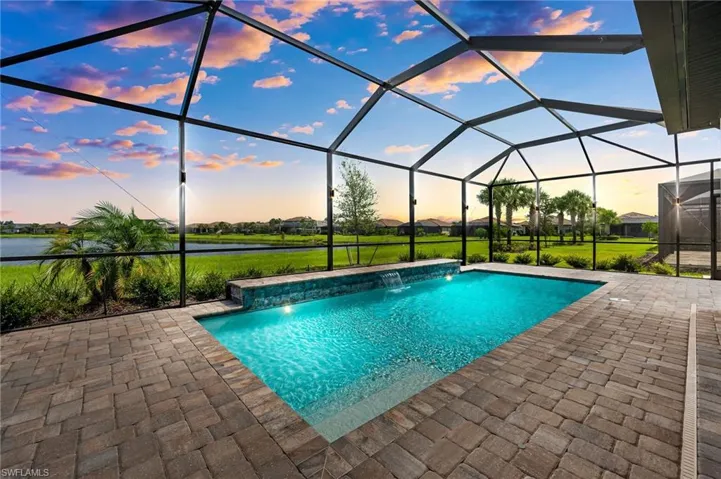 Pool at dusk featuring a water view, pool water feature, a lanai, and a patio area