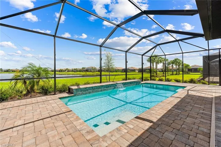View of swimming pool with a lanai, a water view, a lawn, pool water feature, and a patio
