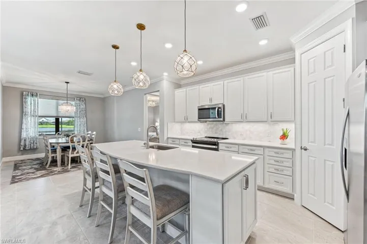 Kitchen with hanging light fixtures, appliances with stainless steel finishes, white cabinetry, sink, and a kitchen island with sink