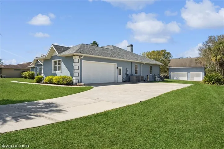 Single story home featuring an attached garage, a shingled roof, concrete driveway, a chimney, and a front yard