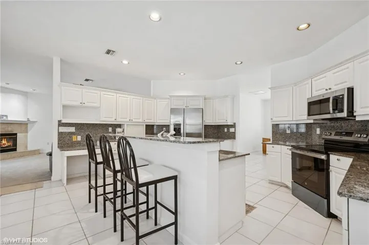 Kitchen featuring new appliances with stainless steel finishes, light tile patterned flooring, dark stone counters, a tile fireplace in the adjacent family room, and a kitchen breakfast bar