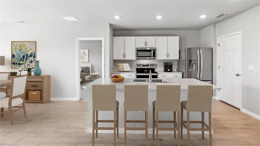 This image is virtually staged. Kitchen featuring stainless steel appliances, white cabinetry, a kitchen island with sink, a kitchen breakfast bar, and light stone counters