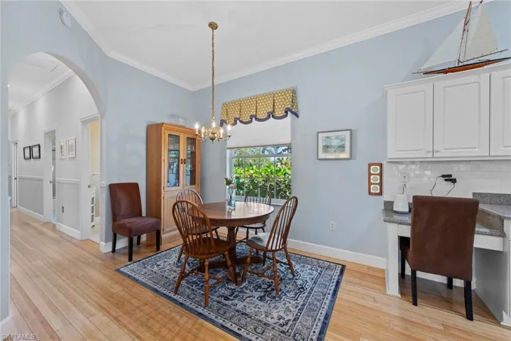 Dining space featuring light wood finished floors, crown molding, baseboards, arched walkways, and a notable chandelier