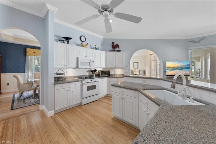 Kitchen featuring white appliances, arched walkways, a sink, crown molding, and light wood-type flooring
