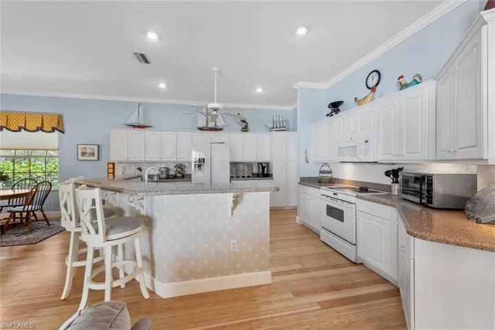 Kitchen featuring white appliances, a breakfast bar area, visible vents, ornamental molding, and light wood-type flooring