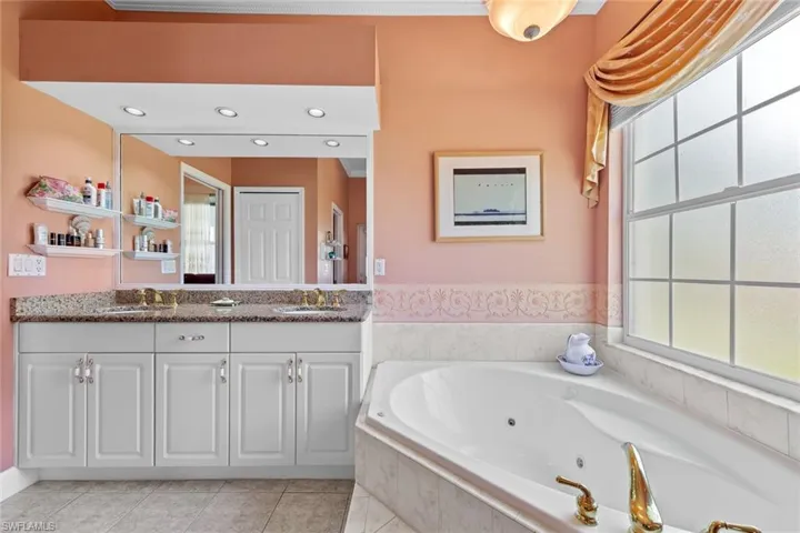 Full bath with tile patterned floors, double vanity, a jetted tub, and a sink