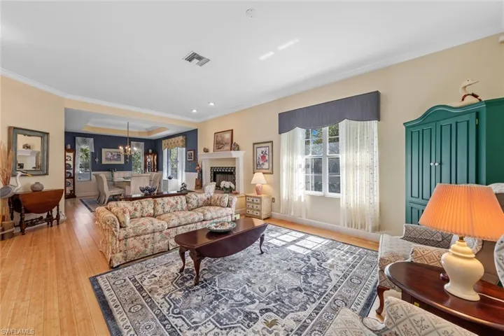 Living room with light wood finished floors, visible vents, crown molding, baseboards, and a notable chandelier