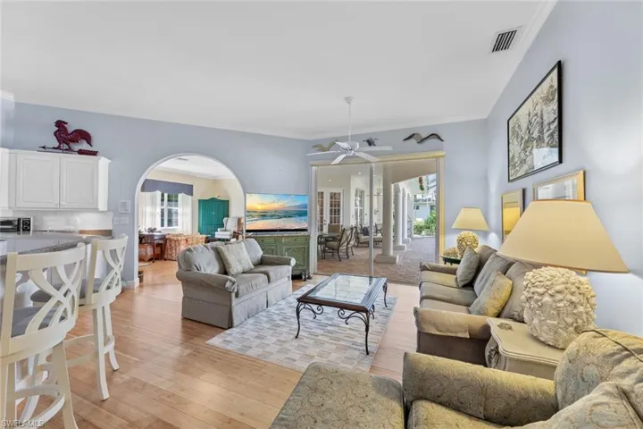 Living area with visible vents, ornamental molding, arched walkways, light wood-style floors, and ceiling fan