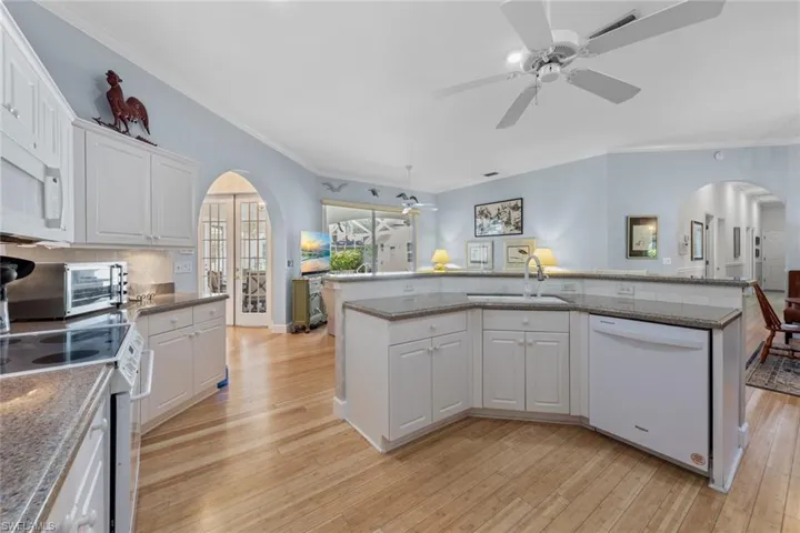 Kitchen featuring white appliances, a ceiling fan, arched walkways, a sink, and light wood-style floors
