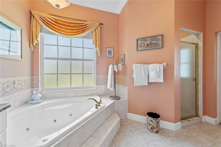 Full bath with a tub with jets, baseboards, a stall shower, crown molding, and tile patterned floors