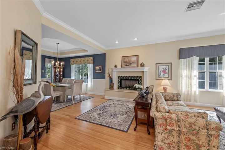 Living room with visible vents, a fireplace with raised hearth, wood finished floors, an inviting chandelier, and crown molding