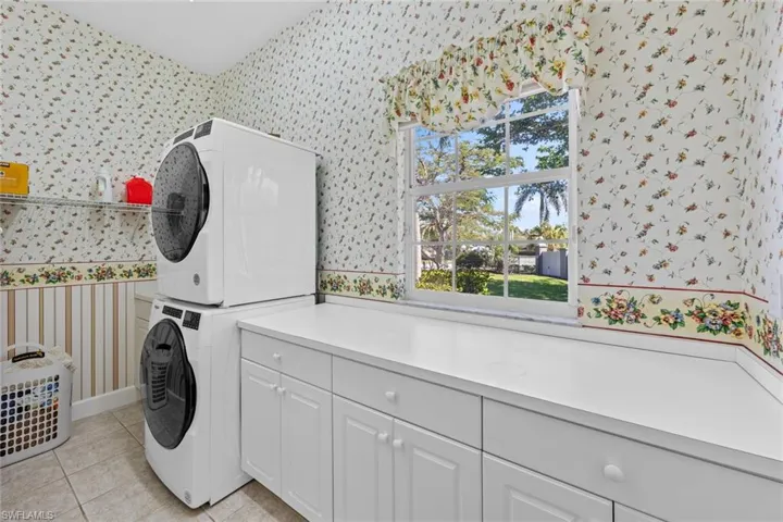 Washroom featuring wallpapered walls, cabinet space, and stacked washer / drying machine