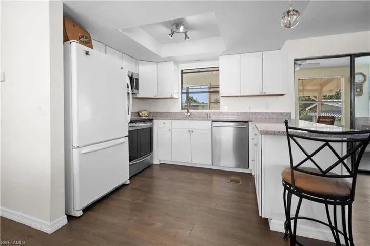 Kitchen with appliances with stainless steel finishes, a tray ceiling, white cabinets, dark wood-type flooring, and a peninsula