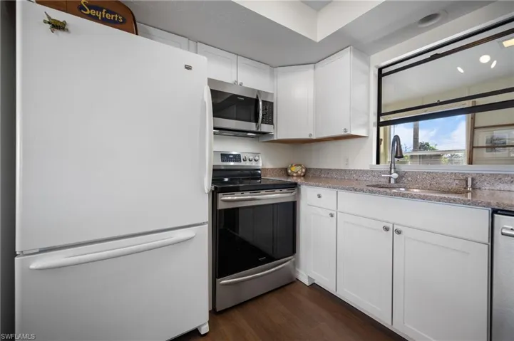Kitchen with stainless steel appliances, white cabinets, dark wood-type flooring, and light stone countertops
