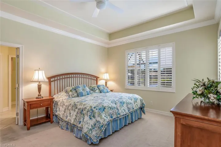 Spacious primary bedroom with a tray ceiling, light carpet, crown molding, door to lanai and a ceiling fan