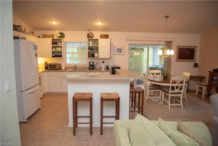 Kitchen featuring a kitchen breakfast bar, a notable chandelier, white cabinetry, light tile patterned floors, and white fridge