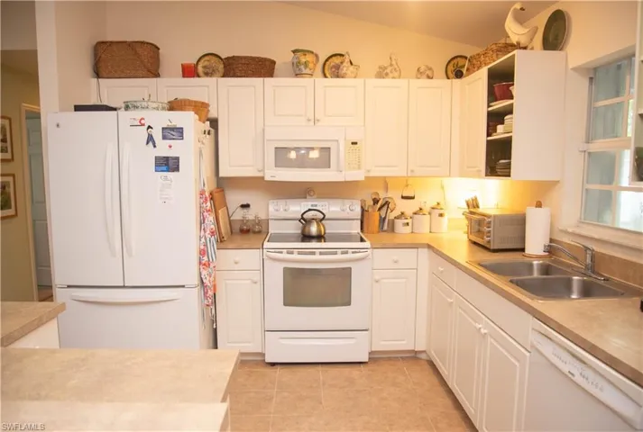 Kitchen featuring lofted ceiling, white cabinetry, light tile patterned floors, white appliances, and sink