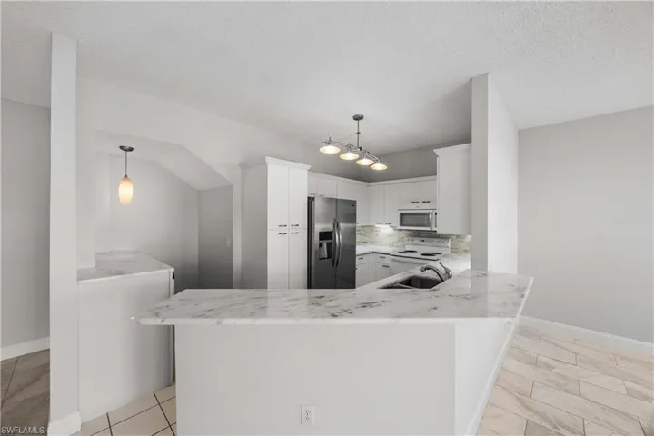 Kitchen featuring a peninsula, stainless steel appliances, decorative backsplash, white cabinetry, and light stone countertops